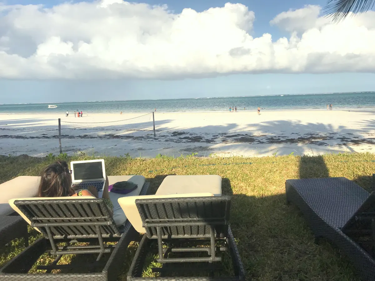 A laptop on a sun lounger looking out over a white sand beach