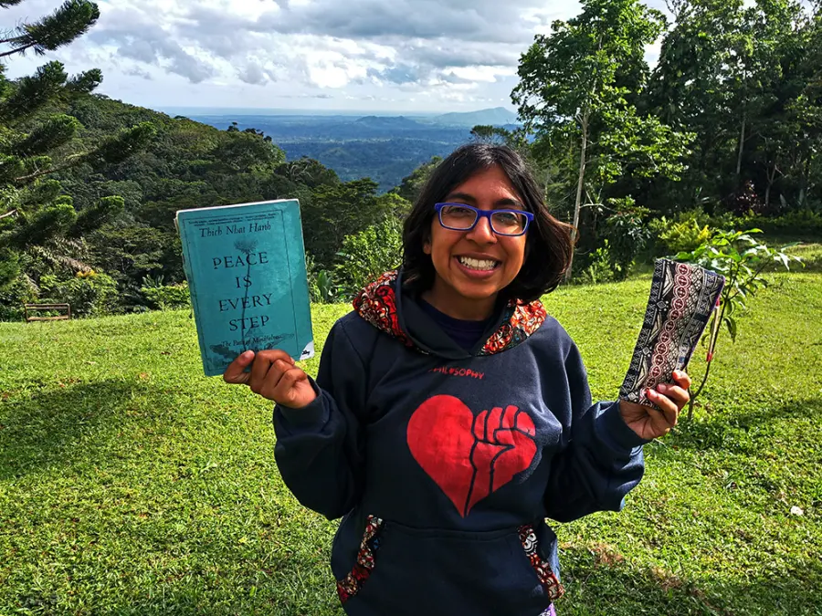 Nari holding a copy of Peace Is Every Step on a green hillside