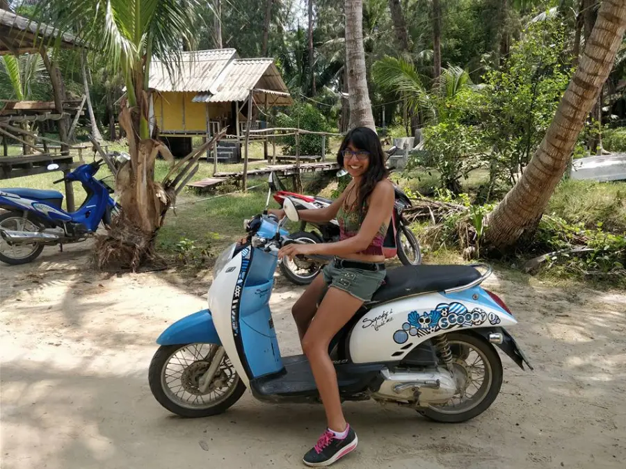 Nari sitting on a scooter among palm trees in Thailand