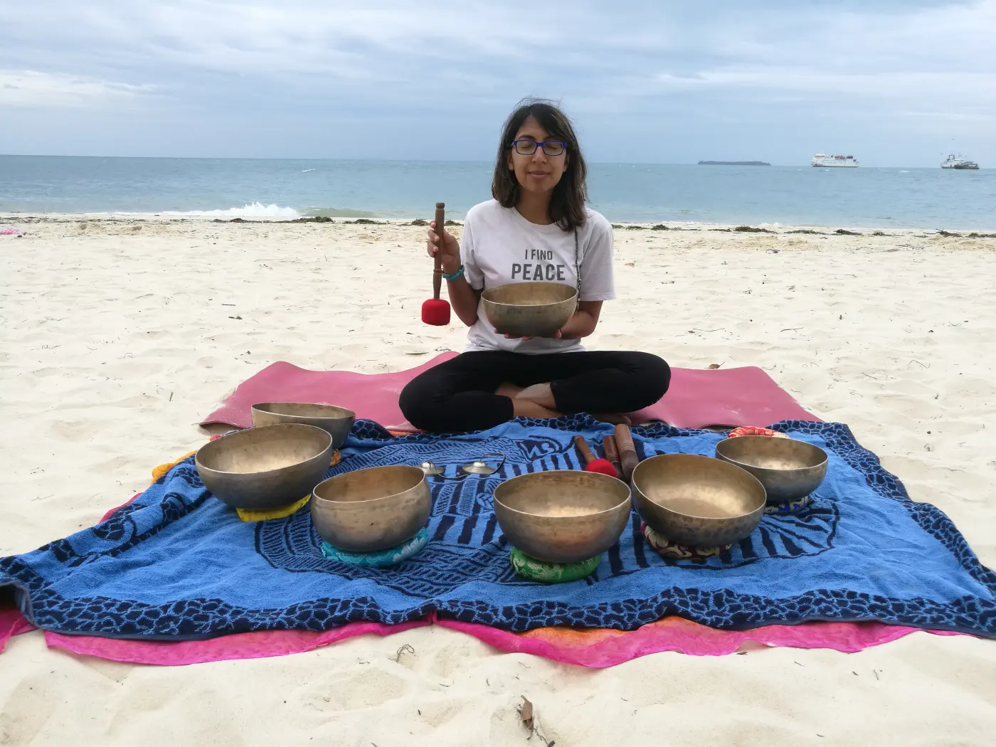 Nari seated with singing bowls on a beach
