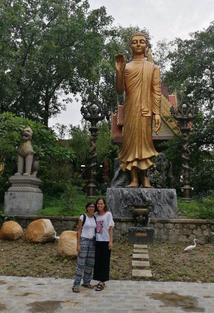 Two ladies standing under a golden Buddha statue wearing tops with sleeves and baggy trousers